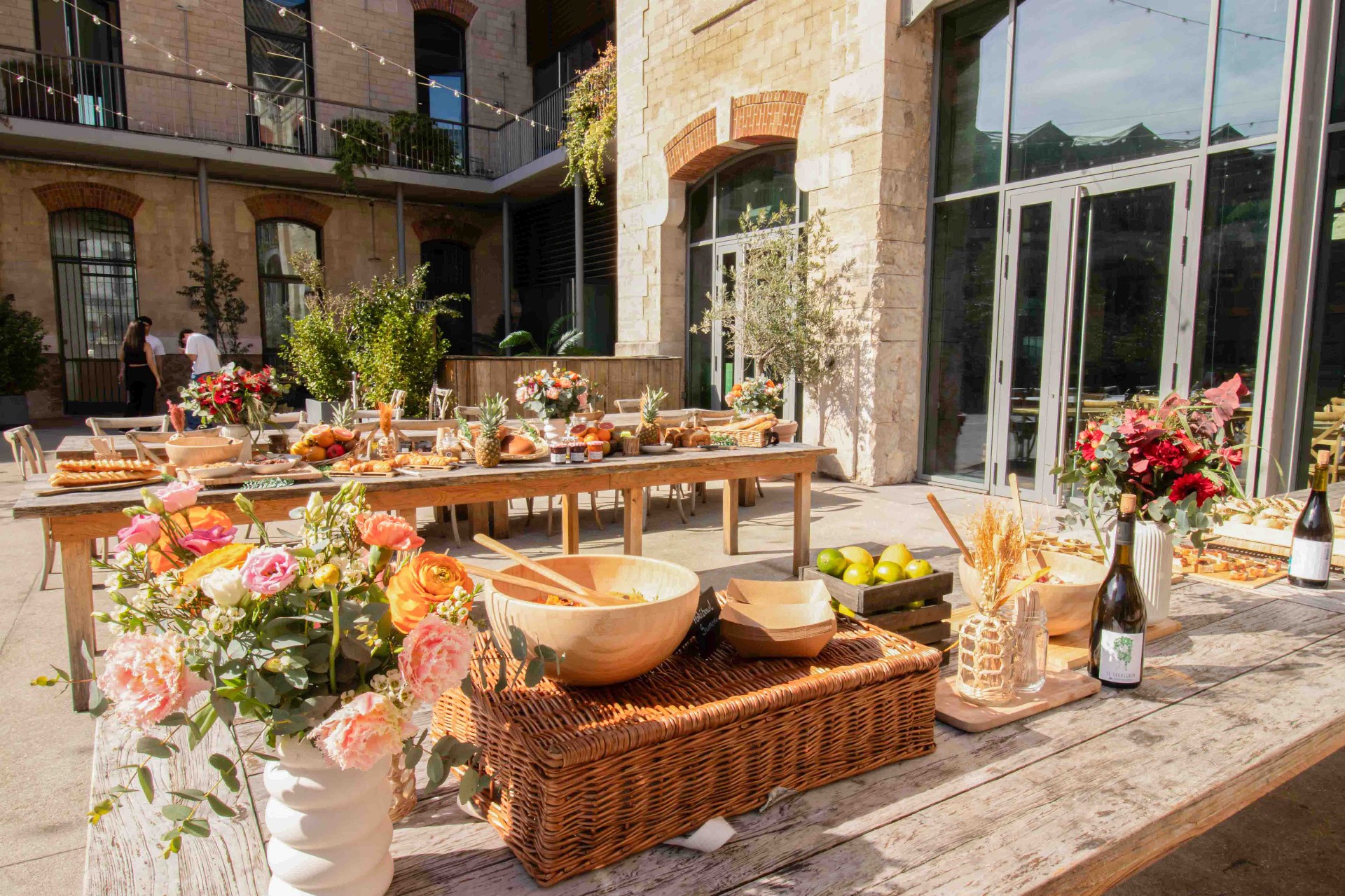 Outdoor courtyard hospitality setup — seasonal buffet, flowers and wine service in a sunlit stone venue